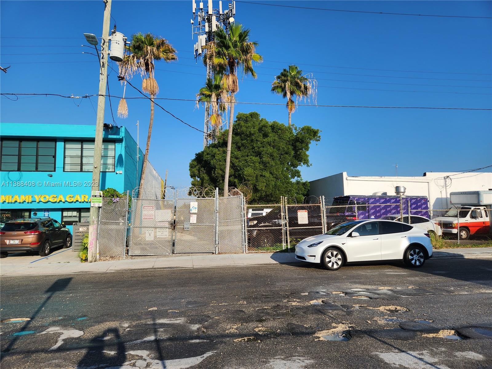 A white Tesla is parked on a street in front of a fenced industrial lot — 60 NW 20th St, Miami FL 33127, MIAMI, FL