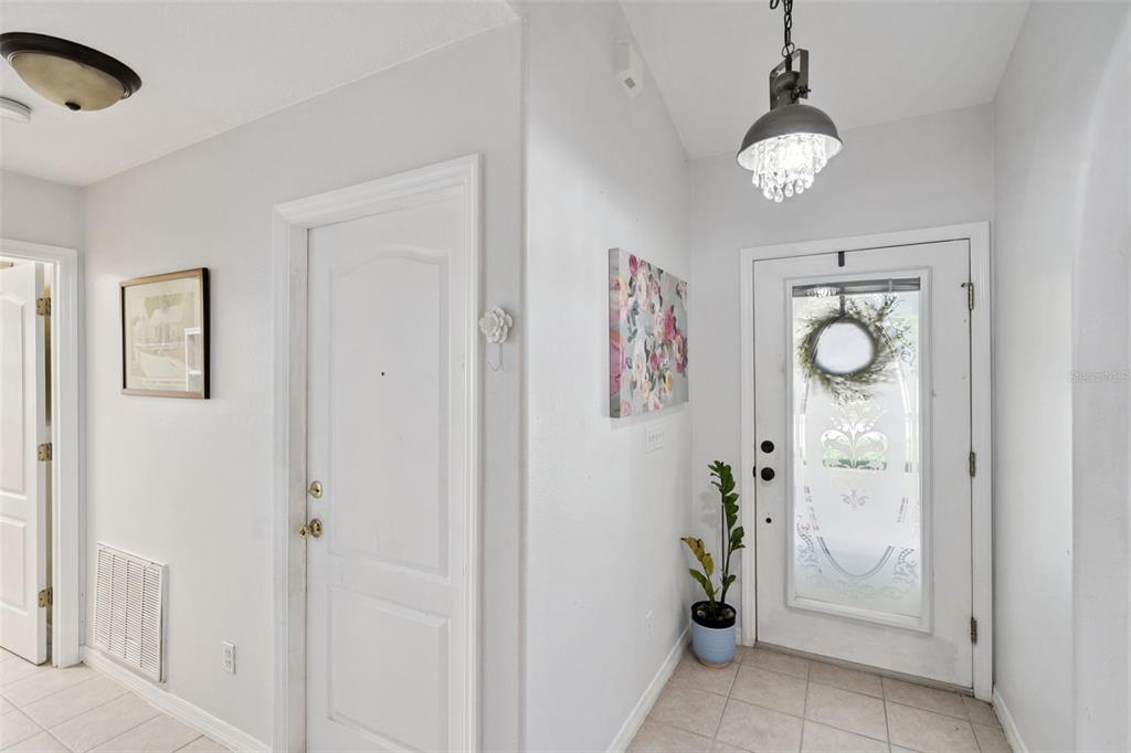 A bright entryway features a white front door, tile flooring, and a hanging pendant light — 8856 COURTYARD LANE, GROVELAND, FL