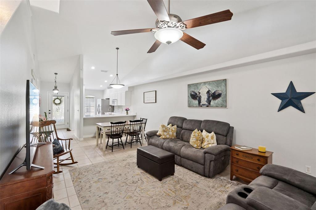 A living room with a grey sofa, a cow painting, and an open-concept dining area — 8856 COURTYARD LANE, GROVELAND, FL