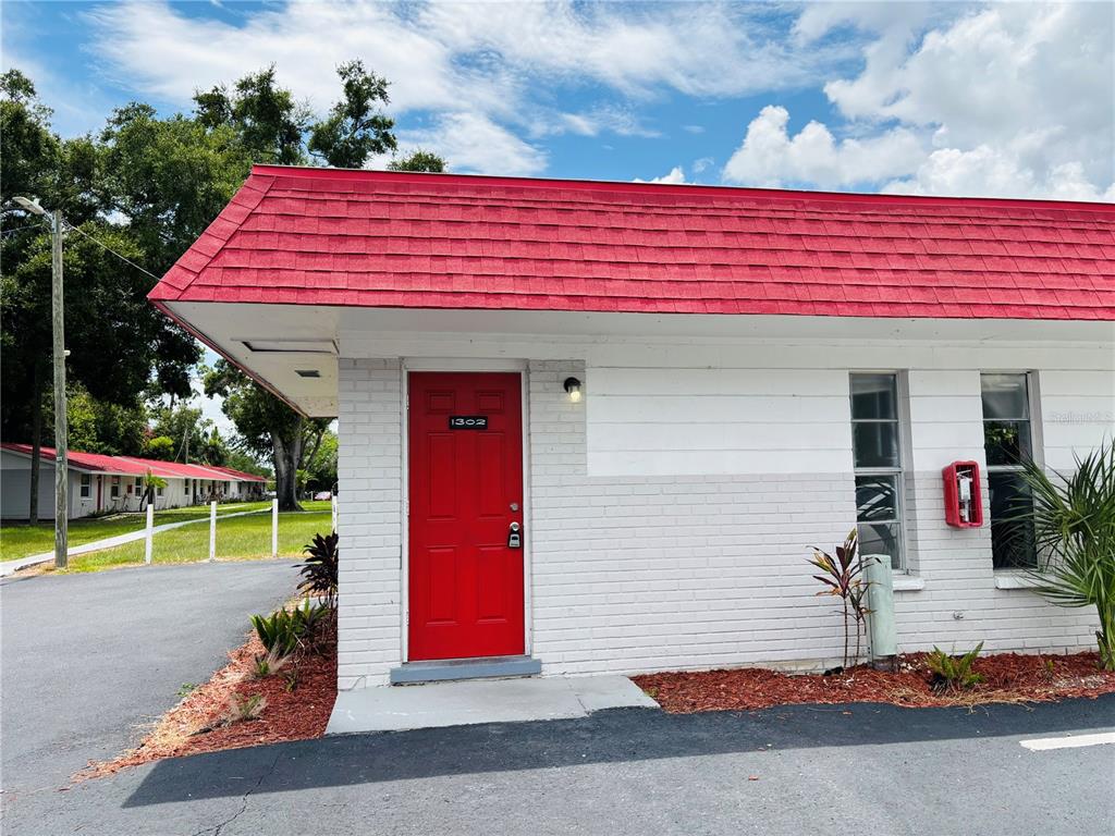 The exterior of a white brick building features a bright red door numbered 1302 — 1302 MORRIS PARK, TAMPA, FL