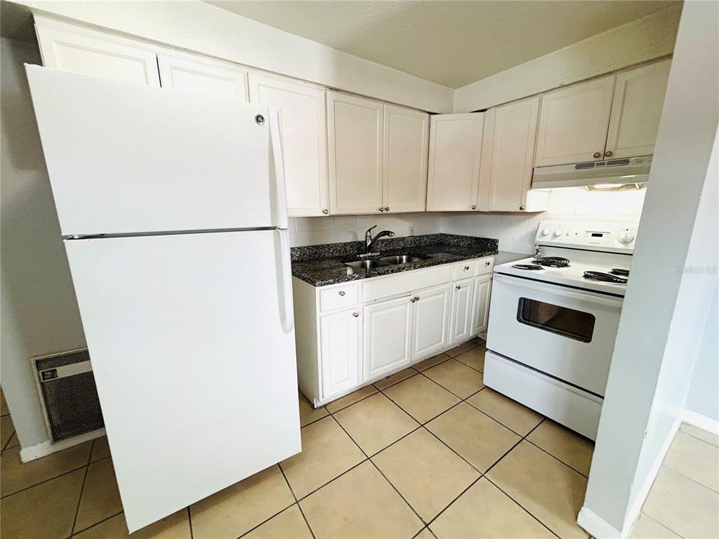 A kitchen features white cabinets, a white refrigerator, a white stove, and dark granite countertops — 1302 MORRIS PARK, TAMPA, FL