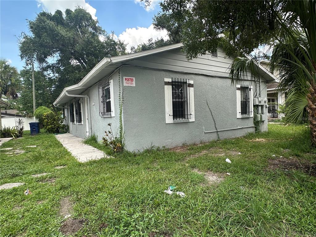 The exterior of a gray, single-story house features barred windows and a posted sign — 8215 N KLONDYKE STREET, TAMPA, FL