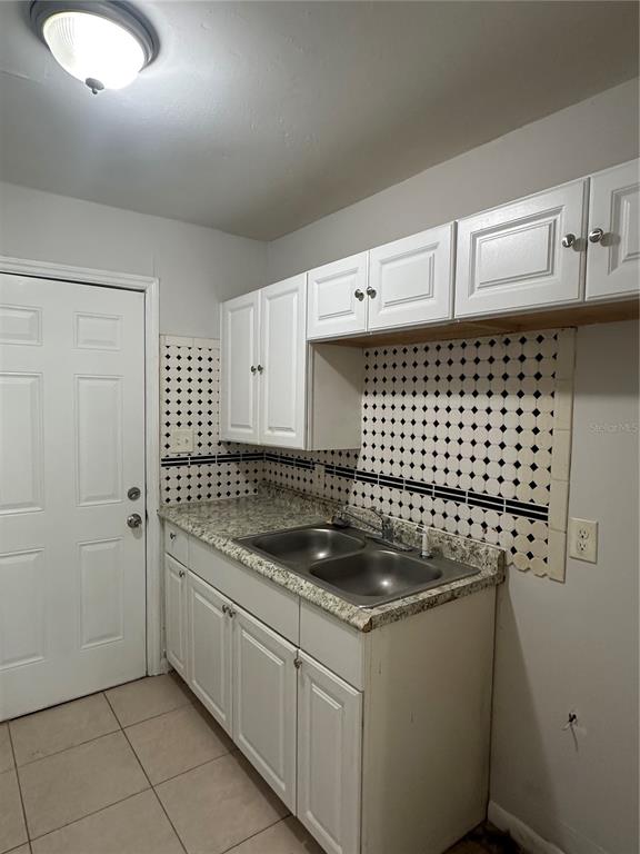 A kitchen features white cabinets, a double-basin stainless steel sink, and a patterned tile backsplash — 8215 N KLONDYKE STREET, TAMPA, FL