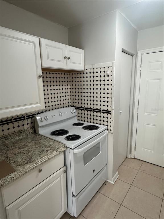 A kitchen features white cabinets, a granite countertop, a white electric stove, and patterned tile — 8215 N KLONDYKE STREET, TAMPA, FL