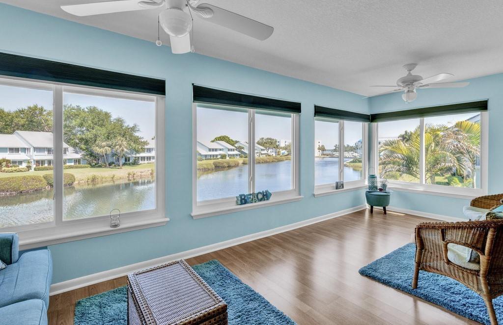 A sunroom with light blue walls, wood flooring, ceiling fans, and large windows overlooking water — 6408 S River Run Drive, Sebastian FL 32958, SEBASTIAN, FL