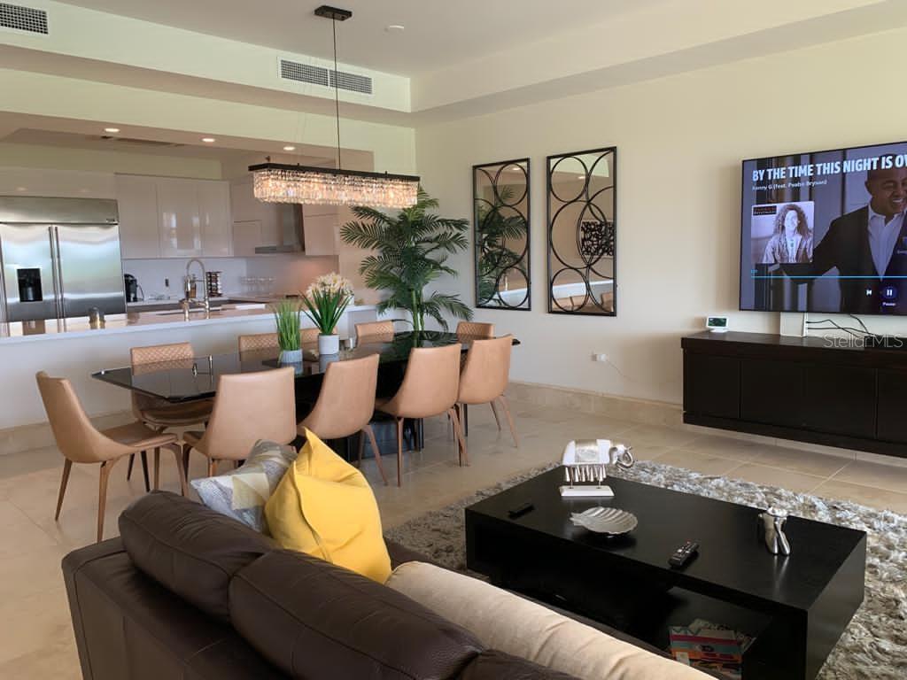 An open-concept living and dining area features a modern kitchen, leather sofa, and television — 500 PLANTATION DR. UNIT 304, DORADO, PR