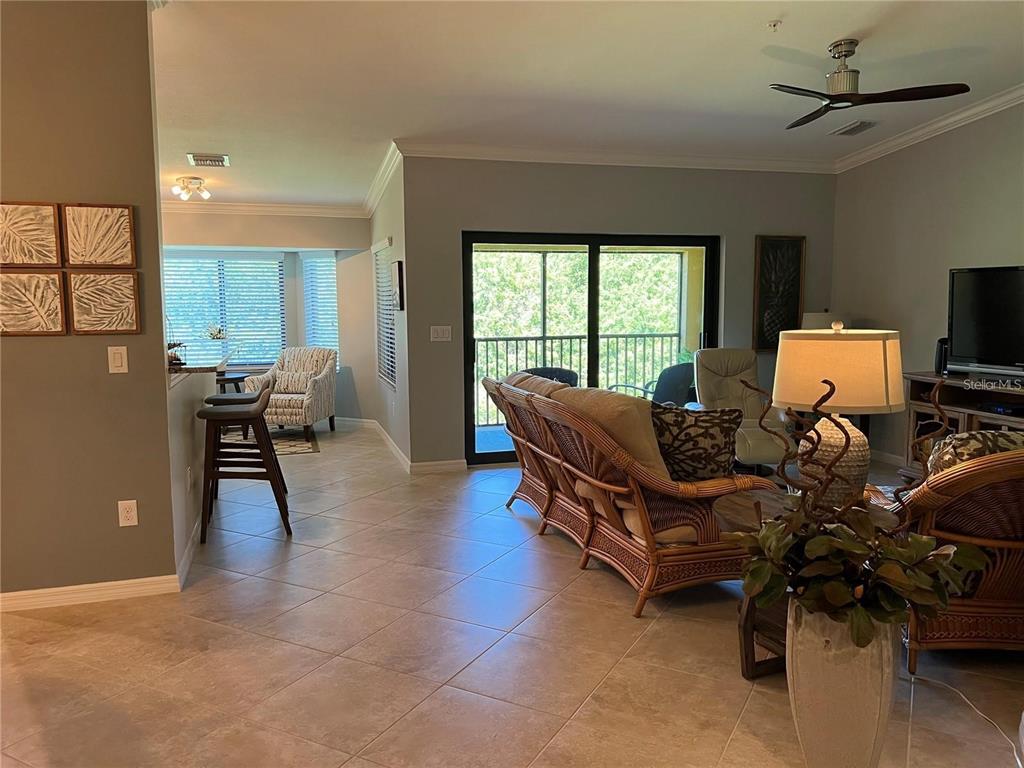 A living room with tile floors, wicker furniture, and a sliding glass door to a balcony — 6611 GRAND ESTUARY TRAIL UNIT 204, BRADENTON, FL