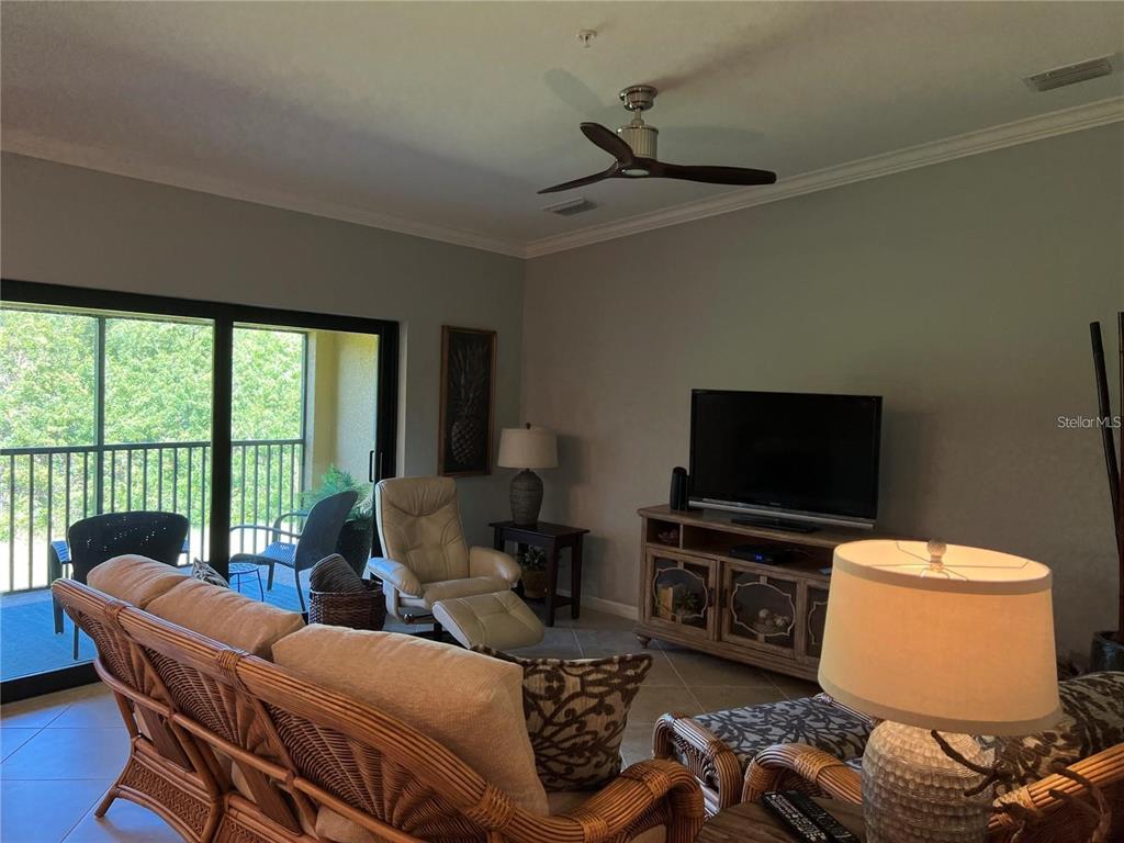 A living room features a wicker sofa, a television console, and a sliding glass door — 6611 GRAND ESTUARY TRAIL UNIT 204, BRADENTON, FL