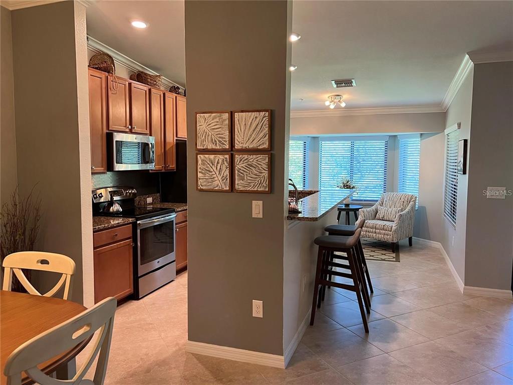 A kitchen with wood cabinets and stainless steel appliances opens to a dining area — 6611 GRAND ESTUARY TRAIL UNIT 204, BRADENTON, FL