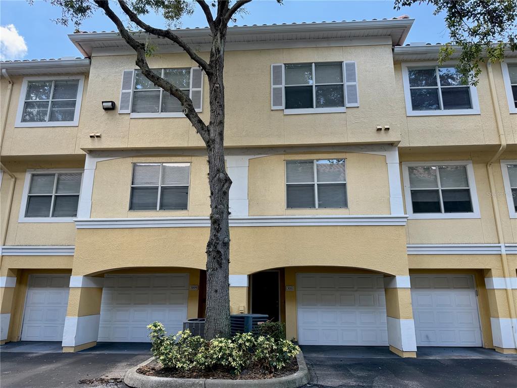 A three-story yellow townhouse exterior features multiple garage doors and a central tree — 3011 LEGACY VILLAS DRIVE UNIT 3011, MAITLAND, FL