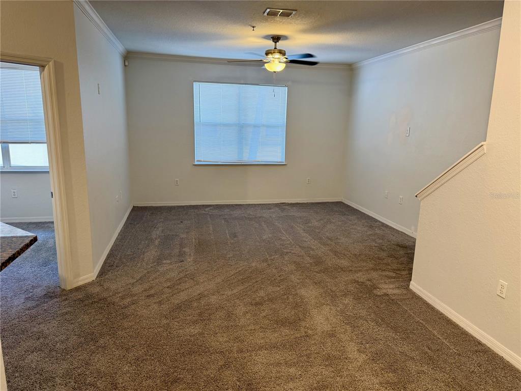 A carpeted living room features a ceiling fan, a window with blinds, and a staircase — 3011 LEGACY VILLAS DRIVE UNIT 3011, MAITLAND, FL