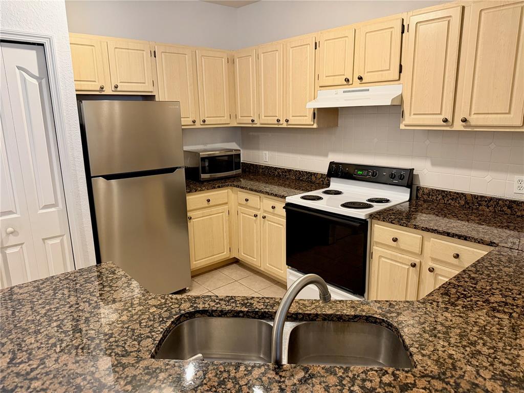 A kitchen features light wood cabinets, granite countertops, a stainless steel refrigerator, and white appliances — 3011 LEGACY VILLAS DRIVE UNIT 3011, MAITLAND, FL