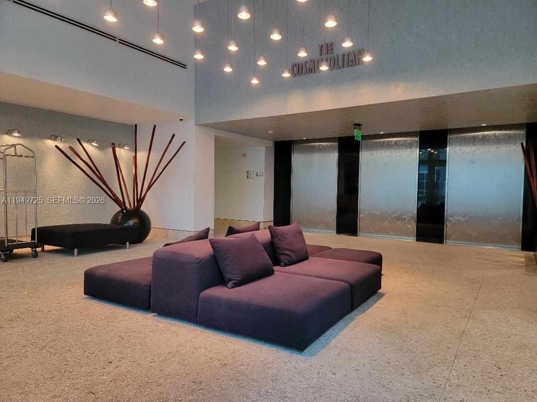 A modern lobby features a purple sectional sofa, hanging pendant lights, and a water feature — 110 Washington Ave # 2310, Miami Beach FL 33139, MIAMI BEACH, FL