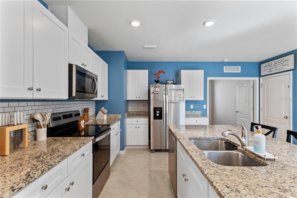 A kitchen features white cabinets, granite countertops, stainless steel appliances, and blue walls — 407 PELHAM PARK DRIVE, DELAND, FL