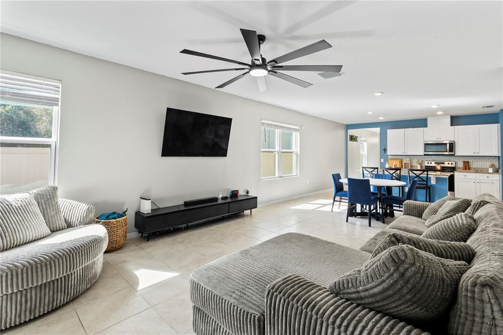 An open-concept living room and kitchen feature tile flooring, a ceiling fan, and gray furniture — 407 PELHAM PARK DRIVE, DELAND, FL