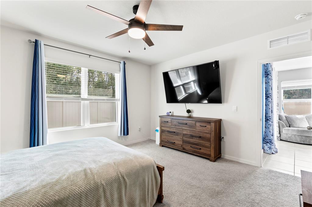 A bedroom features a ceiling fan, a wall-mounted television, a wooden dresser, and carpeted flooring — 407 PELHAM PARK DRIVE, DELAND, FL
