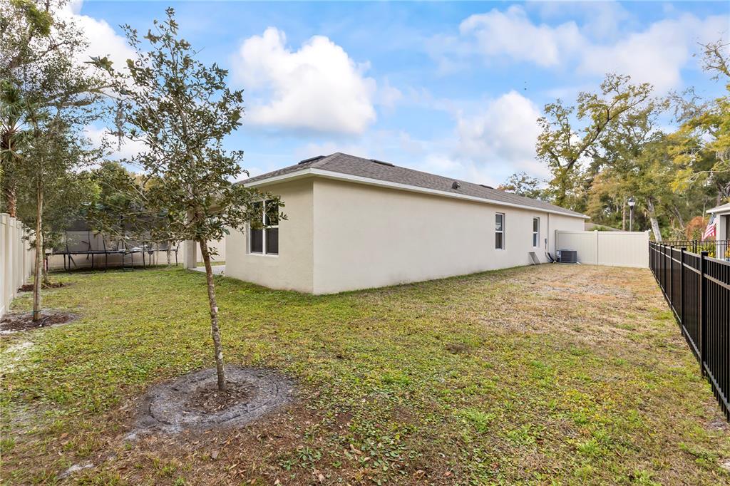 The exterior of a single-story house features a beige stucco finish and a fenced backyard — 407 PELHAM PARK DRIVE, DELAND, FL