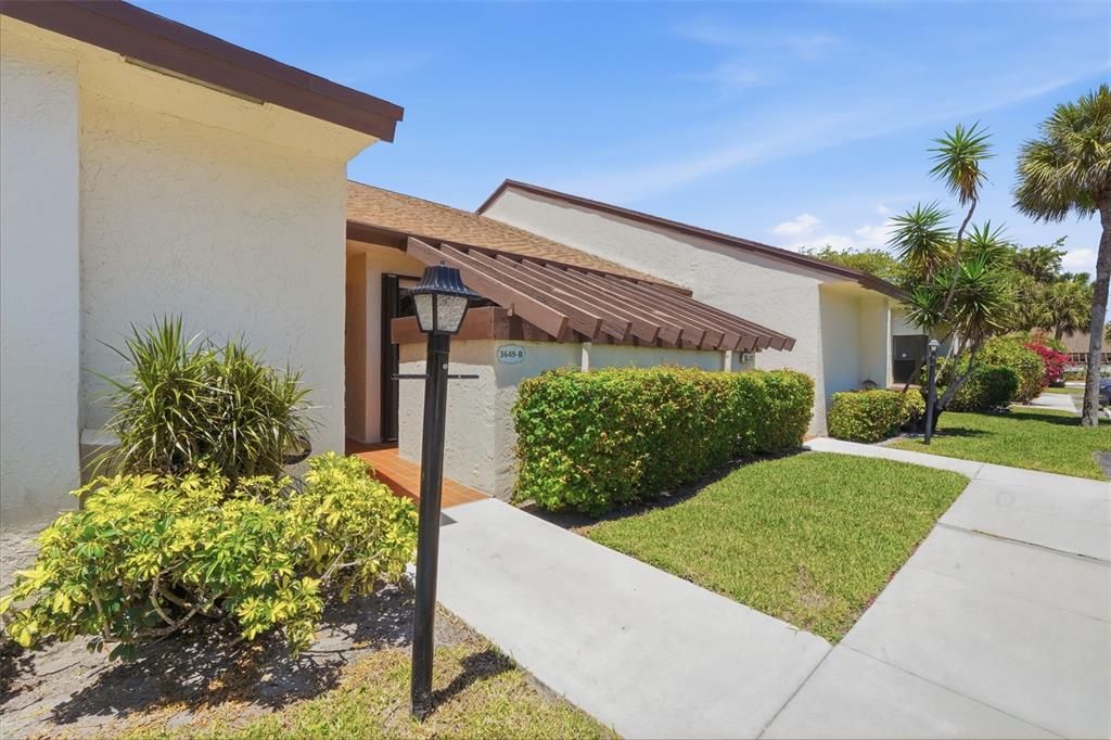 A single-story residential building with a brown roof, stucco walls, and a landscaped front yard — 3649 WASH ROAD UNIT B, LAKE WORTH, FL