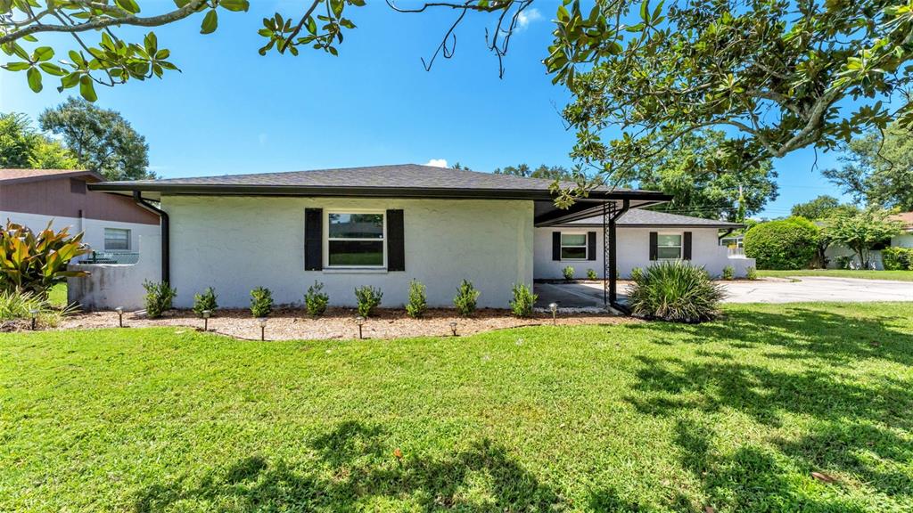 A single-story white house with black shutters and a lawn sits under large trees — 1717 TIERRA ALTA DRIVE, LAKELAND, FL