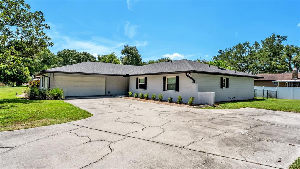 A single-story house with a white exterior, dark roof, and a large cracked concrete driveway — 1717 TIERRA ALTA DRIVE, LAKELAND, FL