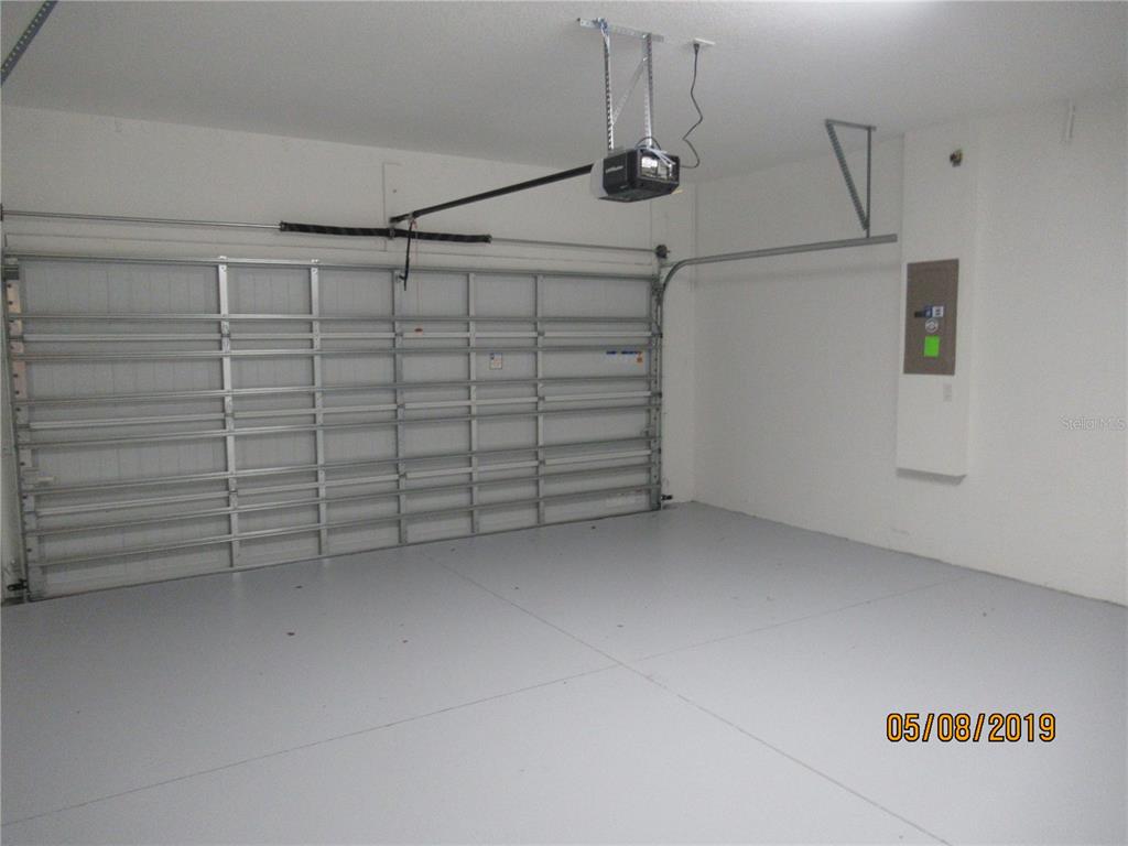 A clean, empty garage features a white sectional door, gray flooring, and a wall-mounted electrical panel — 4606 RHYTHM ROAD, KISSIMMEE, FL