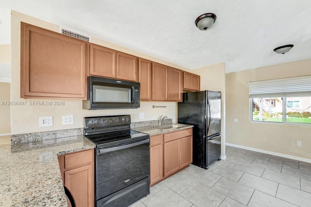 A kitchen features wood cabinets, black appliances, granite countertops, and light-colored tile flooring — 2550 Tulane Ave # 202, Daytona FL 32118, DAYTONA, FL