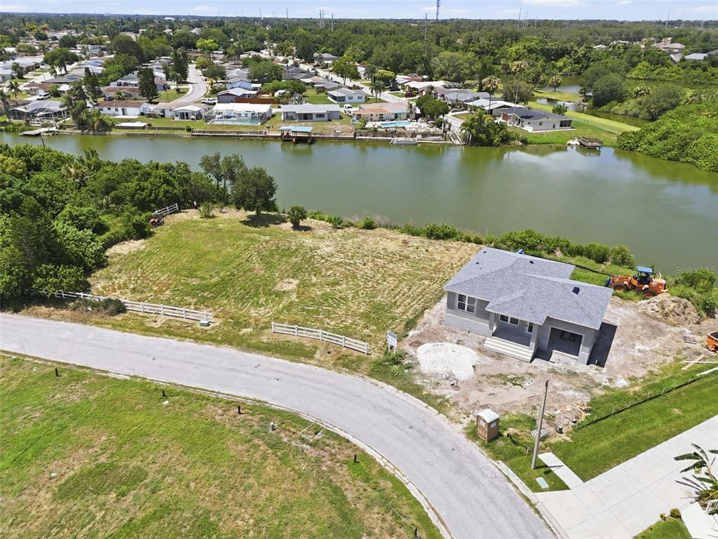 An aerial view shows a newly constructed house on a waterfront lot with a road — 1503 JACKSON DRIVE, HOLIDAY, FL