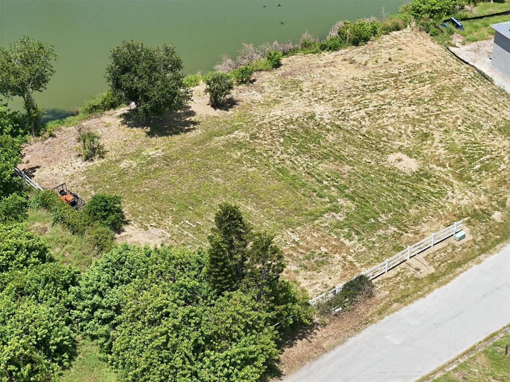 An aerial view shows a vacant, grassy waterfront lot bordered by a white fence — 1503 JACKSON DRIVE, HOLIDAY, FL