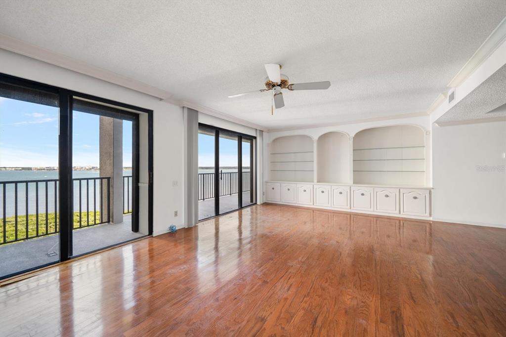 An empty living room features hardwood floors, a ceiling fan, and built-in wall shelving — 1501 GULF BOULEVARD UNIT 604, CLEARWATER BEACH, FL
