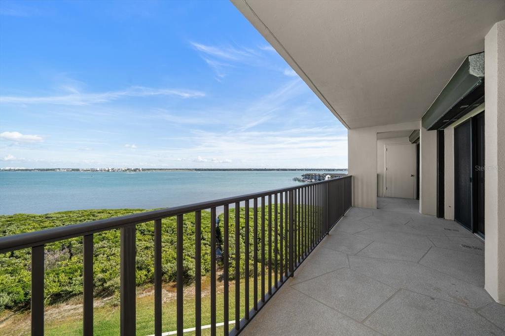 A covered balcony with a metal railing overlooks a coastal view of water and vegetation — 1501 GULF BOULEVARD UNIT 604, CLEARWATER BEACH, FL