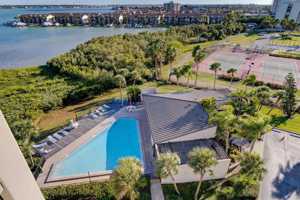 An aerial view shows a swimming pool, a clubhouse, tennis courts, and a waterfront complex — 1501 GULF BOULEVARD UNIT 604, CLEARWATER BEACH, FL