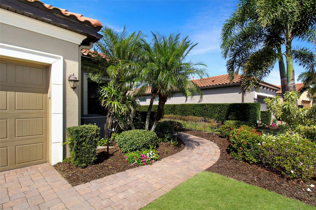 A paved walkway leads past a palm tree and landscaping toward the garage of a house — 5336 VACCARO COURT, BRADENTON, FL