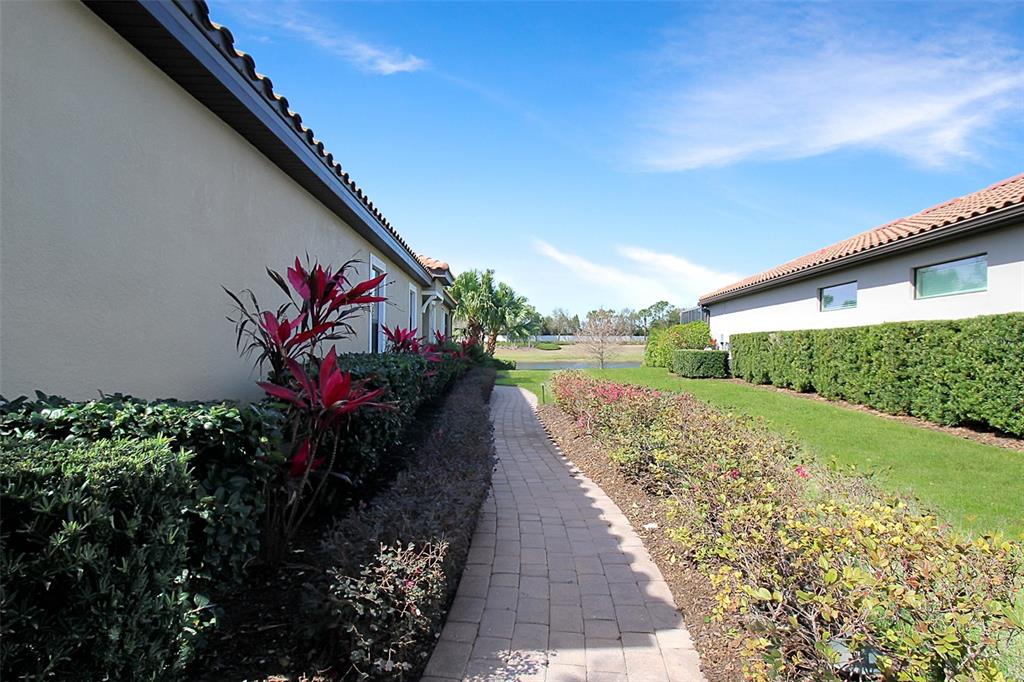 A paved walkway leads between two houses with landscaped hedges and a view of water — 5336 VACCARO COURT, BRADENTON, FL