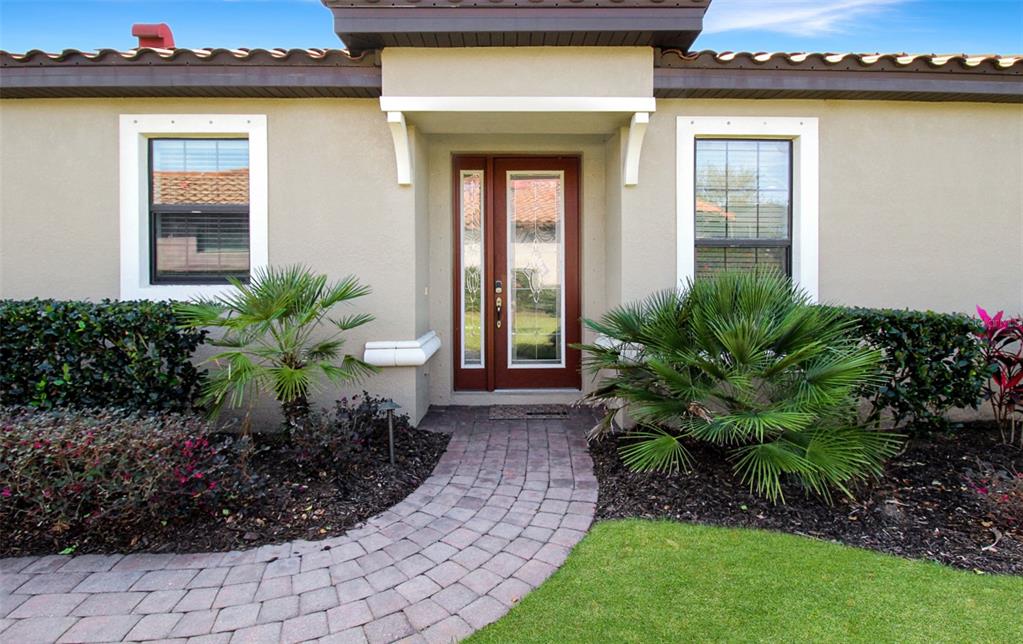 A front exterior view of a house featuring a brick walkway, palm plants, and entryway — 5336 VACCARO COURT, BRADENTON, FL