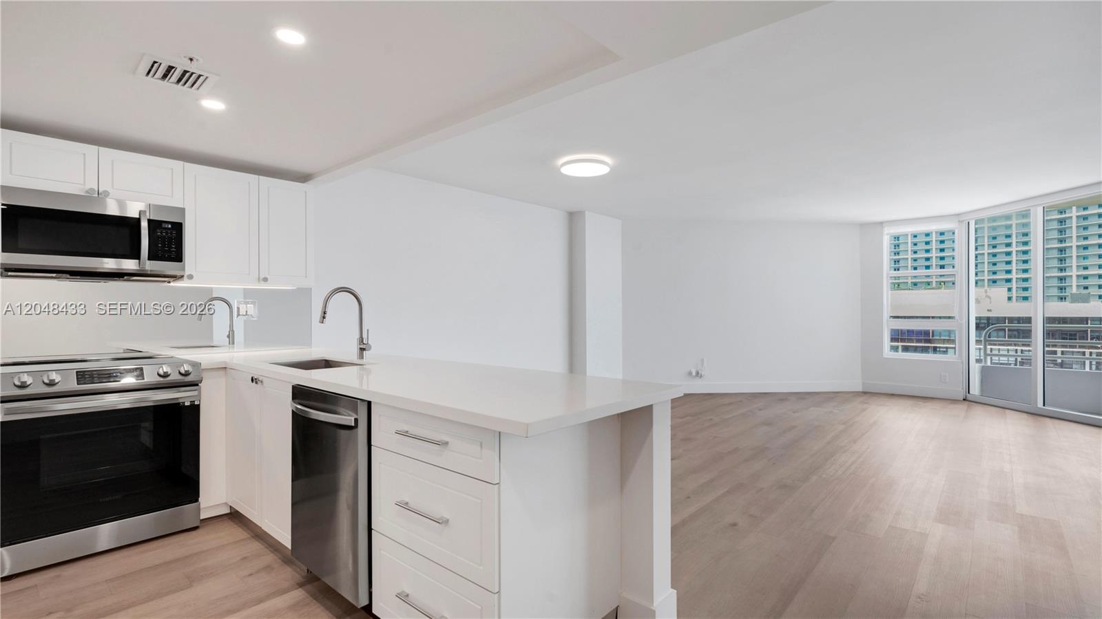 A modern kitchen with white cabinetry and stainless steel appliances opens into a living area — 555 NE 34th St # 2108, Miami FL 33137, MIAMI, FL