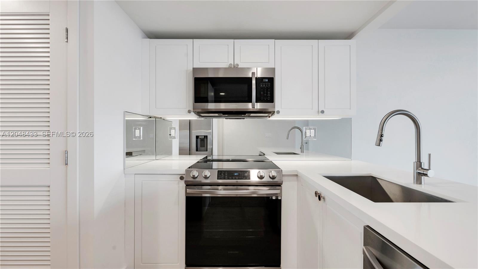 A modern kitchen features white cabinetry, stainless steel appliances, and a mirrored backsplash — 555 NE 34th St # 2108, Miami FL 33137, MIAMI, FL