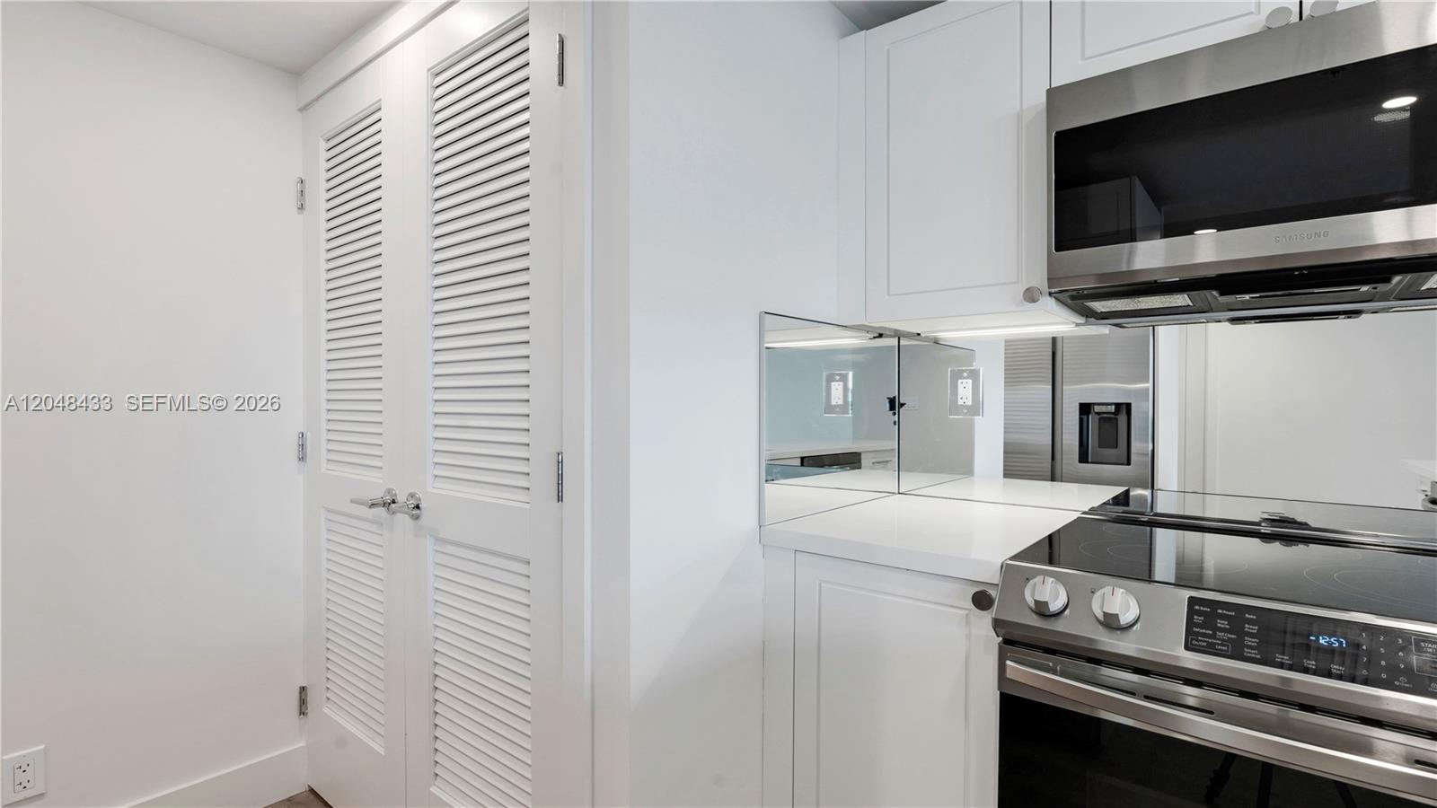 A kitchen features white cabinets, stainless steel appliances, a mirrored backsplash, and louvered closet doors — 555 NE 34th St # 2108, Miami FL 33137, MIAMI, FL