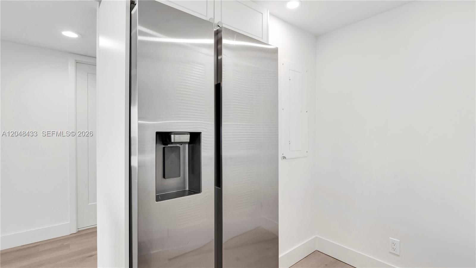 A stainless steel side-by-side refrigerator stands in a white kitchen with light wood flooring — 555 NE 34th St # 2108, Miami FL 33137, MIAMI, FL