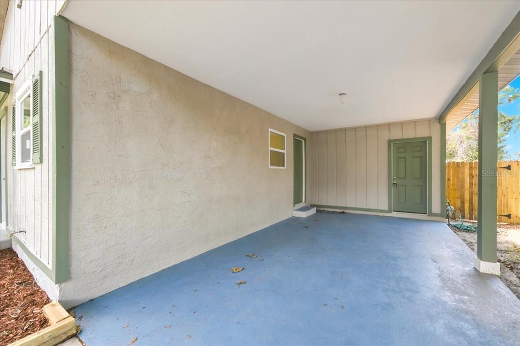 A covered concrete patio features a beige stucco wall, a green door, and vertical siding — 1528 S MADISON AVENUE, CLEARWATER, FL