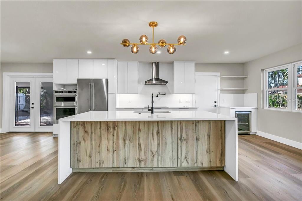 A modern kitchen features a wood-paneled island, white cabinetry, stainless steel appliances, and wood flooring — 525 LAMARA WAY NE, ST PETERSBURG, FL