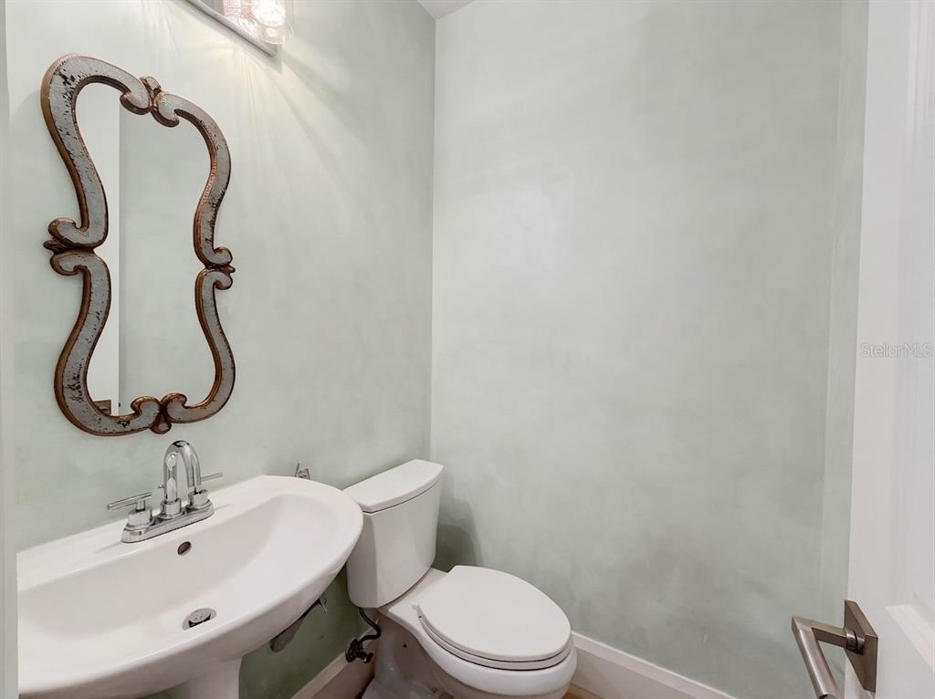 A powder room features a pedestal sink, a toilet, and a decorative mirror on walls — 6772 SOUTHERN OAK COURT, NAPLES, FL