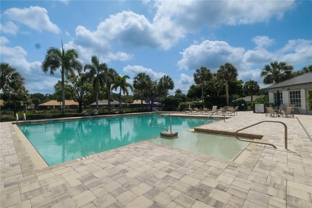 A rectangular swimming pool with a shallow entry area is surrounded by a paved deck — 6772 SOUTHERN OAK COURT, NAPLES, FL