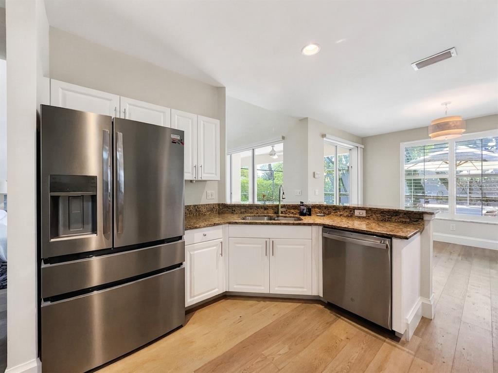 A kitchen features white cabinets, granite countertops, stainless steel appliances, and light wood flooring — 6772 SOUTHERN OAK COURT, NAPLES, FL