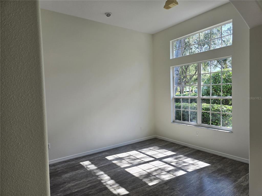 An empty room with light-colored walls, dark wood-look flooring, and large windows with transoms — 8427 SAILING LOOP, LAKEWOOD RANCH, FL
