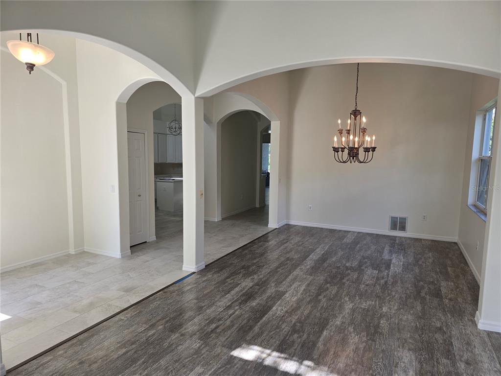 An open-concept dining area with wood-look flooring, arched entryways, and a hanging chandelier — 8427 SAILING LOOP, LAKEWOOD RANCH, FL