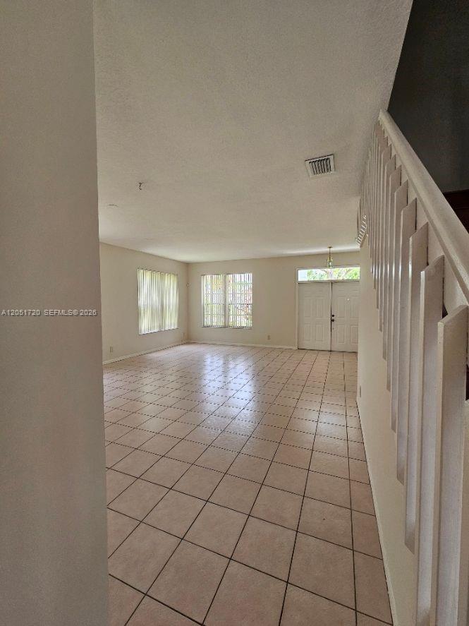 An empty living room features light-colored tile flooring and a staircase with white railings — 7558 Prescott Ln, Lake Worth FL 33467, LAKE WORTH, FL