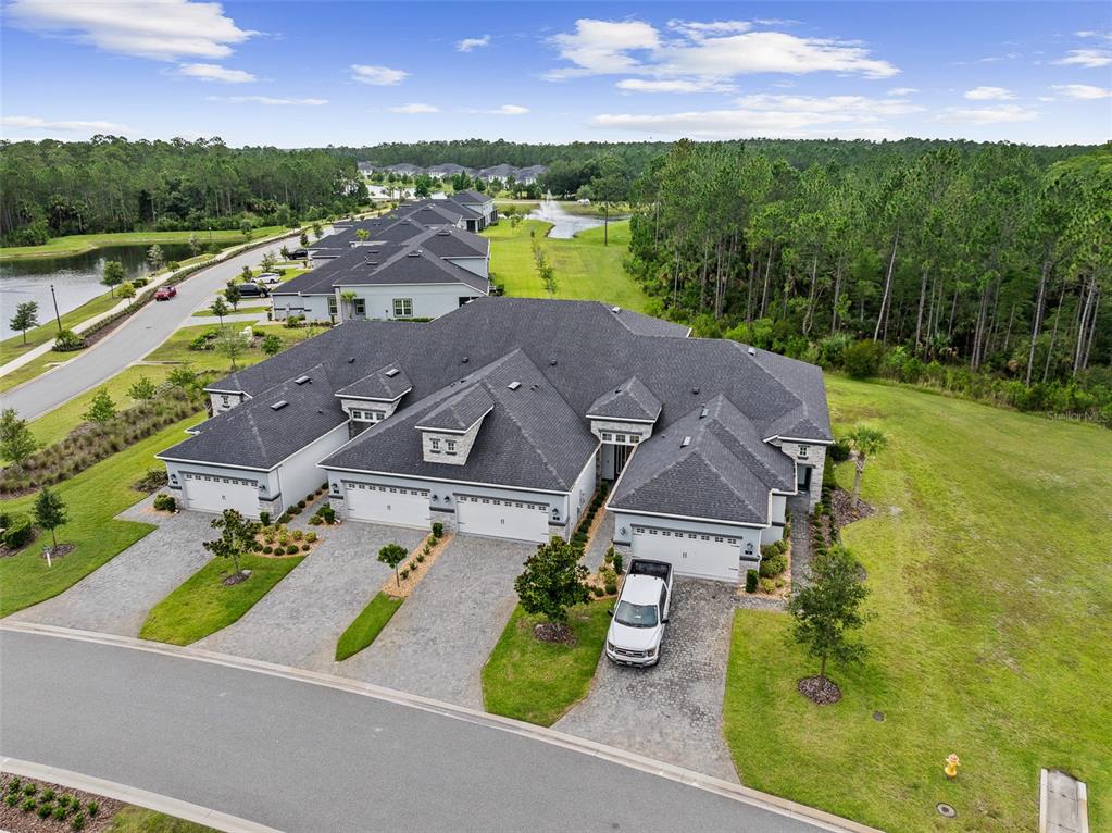 An aerial view shows a multi-unit residential building with gray roofs and paved driveways — 7 NEWHAVEN LANE, ORMOND BEACH, FL