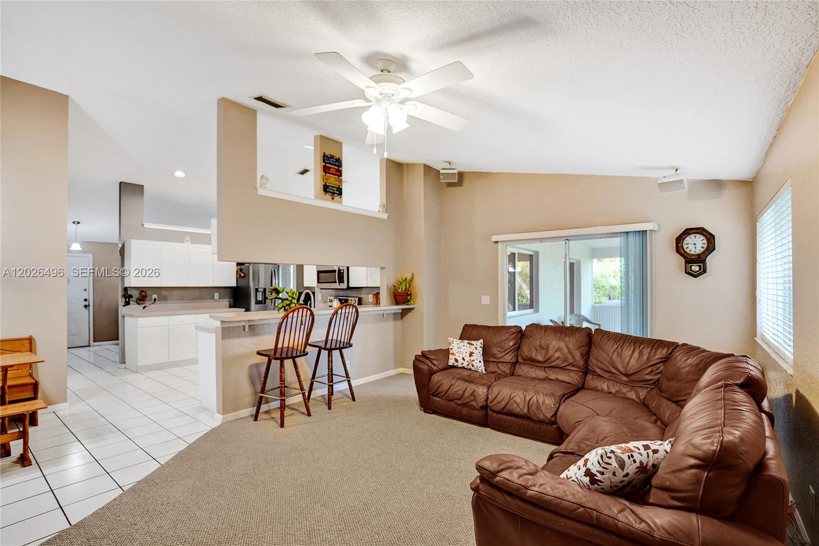 A living room with a brown sectional sofa, carpeted floor, and an open kitchen area — 14808 N 69th St N, Loxahatchee FL 33470, LOXAHATCHEE, FL
