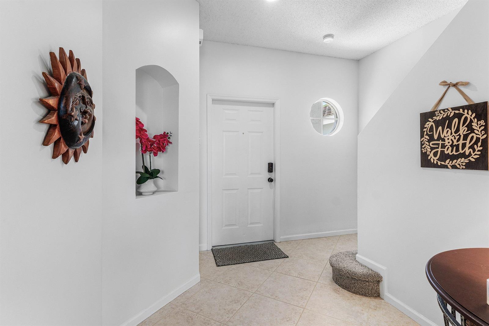 An entryway features a white door, a recessed wall niche with flowers, and a staircase — 7874 Sienna Springs Drive, Lake Worth FL 33463, LAKE WORTH, FL