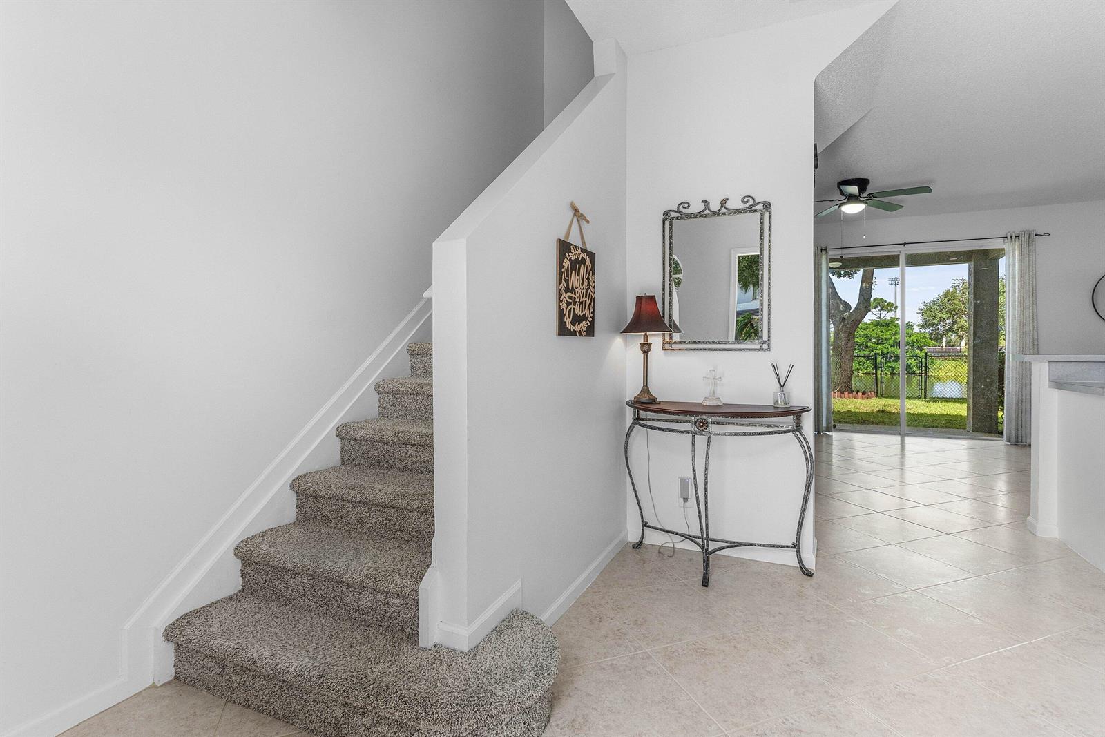 An entryway features a carpeted staircase, a console table with a mirror, and tiled flooring — 7874 Sienna Springs Drive, Lake Worth FL 33463, LAKE WORTH, FL